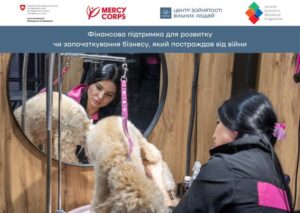 Зображення, яке показує жінку-грумера, що працює з собакою, що символізує успішний запуск або розвиток бізнесу в умовах війни. Зверху розташовані логотипи Програми підтримки економічної стійкості, ГО «Центр зайнятості Вільних людей» та Mercy Corps, а також текст: "Фінансова підтримка для розвитку чи започаткування бізнесу, який постраждав від війни"