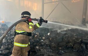 Пожежник у захисному костюмі гасить залишки пожежі на складі каністр та посуду