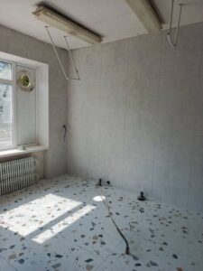 Нова світло-сіра плитка на стінах та підлозі у харчоблоці гімназії. Видно вікно та нову радіаторну батарею.