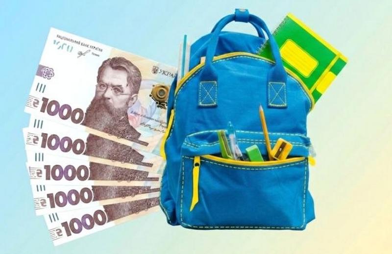 Синій шкільний рюкзак із канцелярським приладдям, зошитами та п'ятьма купюрами по 1000 гривень, що символізують виплату «Пакунок школяра» від держави.