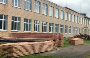 Фасад Ніжиловицької гімназії, біля якого складені дерев'яні бруси та дошки для ремонту покрівлі.