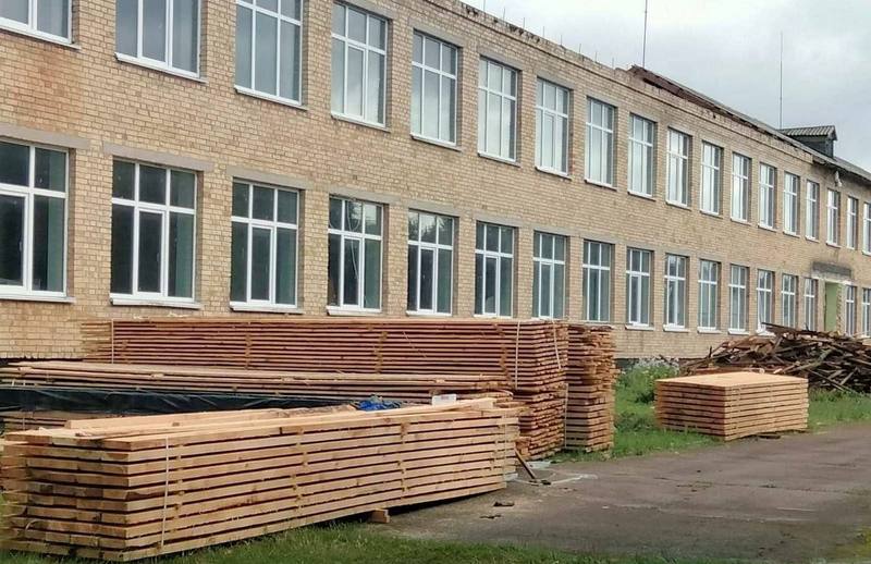 Фасад Ніжиловицької гімназії, біля якого складені дерев'яні бруси та дошки для ремонту покрівлі.