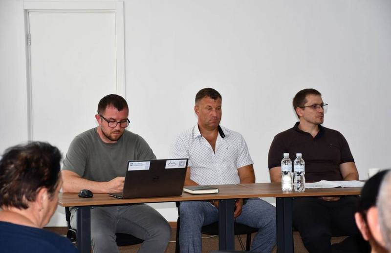 Троє чоловіків — представники селищної ради та консультанти проєкту — сидять за робочим столом із ноутбуком та занотовують пропозиції мешканців.