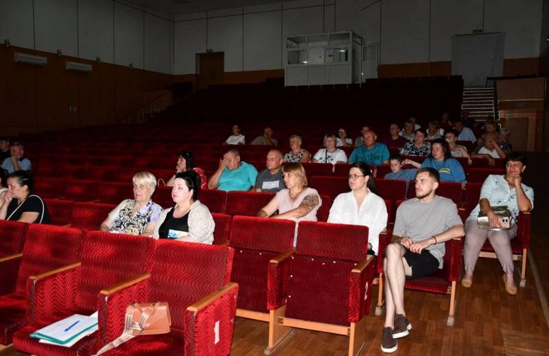 Жителі громади різного віку сидять у червоних кріслах актової зали та слухають інформацію про порядок проведення технічної оцінки житла.