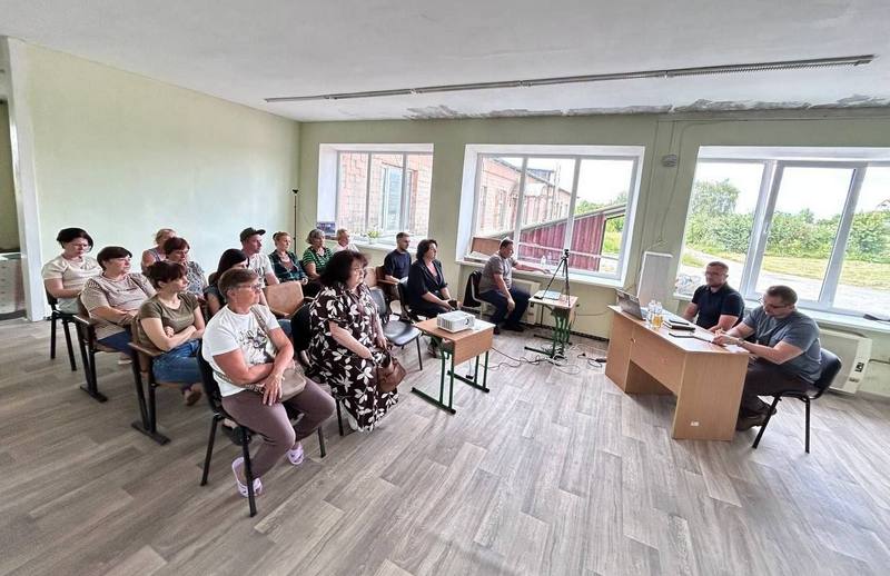 Зустріч у світлій кімнаті: за робочим столом сидять представники ради та проєкту з ноутбуком, навпроти них на стільцях розмістилися мешканці та уважно слухають розповідь.