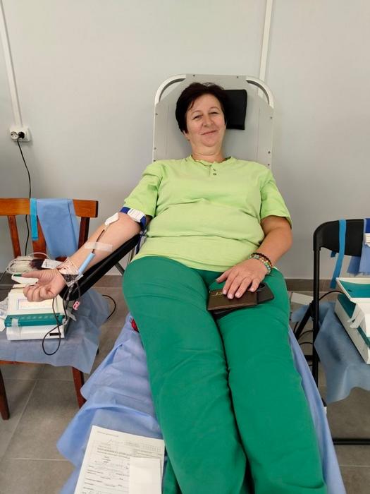 Донорка у світло-зеленій футболці та бірюзових штанах лежить у медичному кріслі. До її руки під'єднано систему для донації крові.