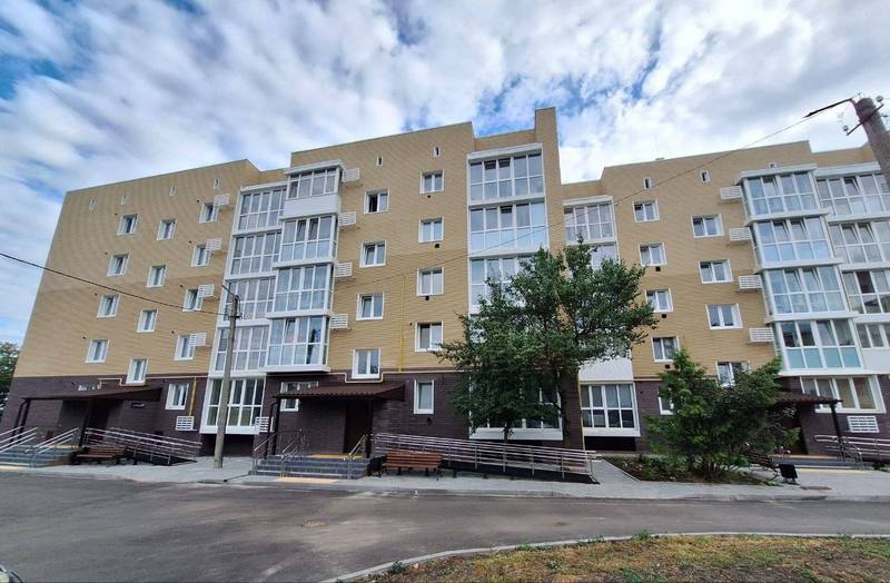 Повний вид на відновлений багатоквартирний будинок у Макарові після ремонту. Фасад утеплений та оздоблений у світло-бежевих та темно-коричневих тонах. Видно нові балкони з панорамним склінням та охайну прибудинкову територію під хмарним небом.