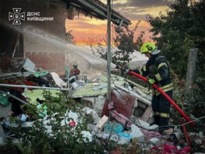 Вогнеборець у захисному спорядженні гасить водою палаючі залишки приватного будинку, зруйнованого внаслідок ворожого обстрілу.