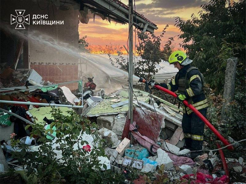 Вогнеборець у захисному спорядженні гасить водою палаючі залишки приватного будинку, зруйнованого внаслідок ворожого обстрілу.