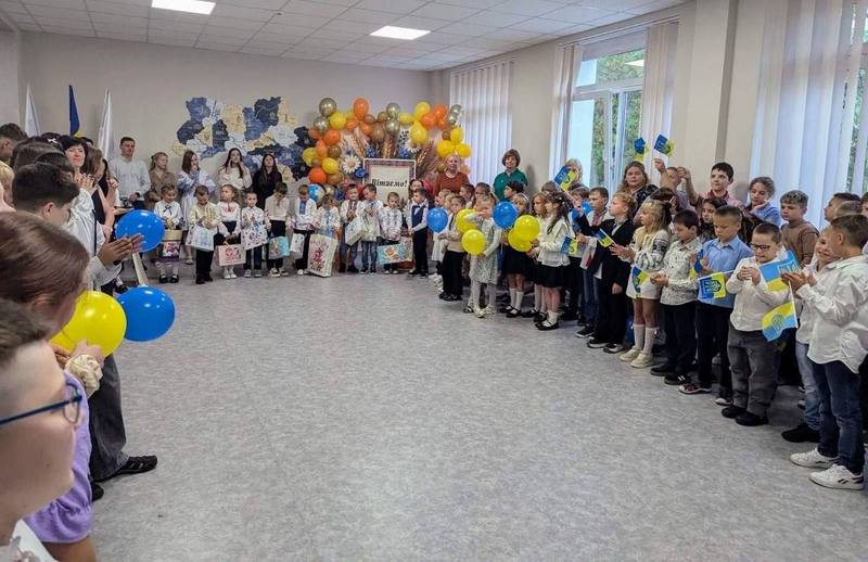 Школярі з синьо-жовтими прапорцями та повітряними кульками на урочистій зустрічі у холі школи