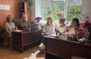 Кілька фахівчинь сидять за робочими столами в кабінеті. На столах є комп'ютер та документи, що демонструє процес надання допомоги ветеранам та їхнім сім'ям.